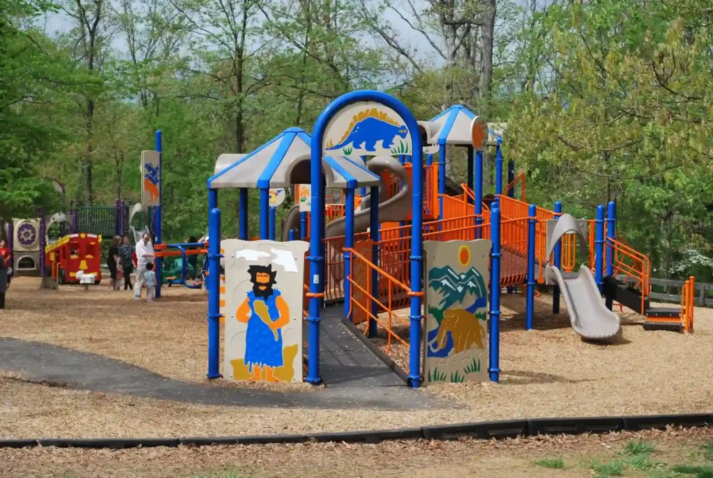 Colorful playground structure with slides and climbing frames surrounded by trees and wood chips on the ground, located in Ashburn Park.