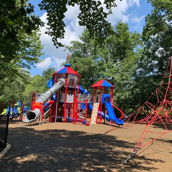 Trailside Park's colorful playground, complete with slides and climbing structures, is surrounded by lush greenery on a sunny day.